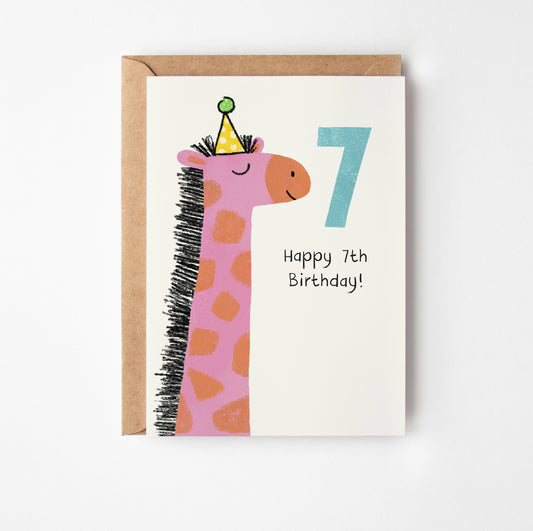 A greeting card with a kraft envelope, featuring a cute pink giraffe wearing a party hat next to a large number 7 and the text 'Happy 7th Birthday!' on a white card.